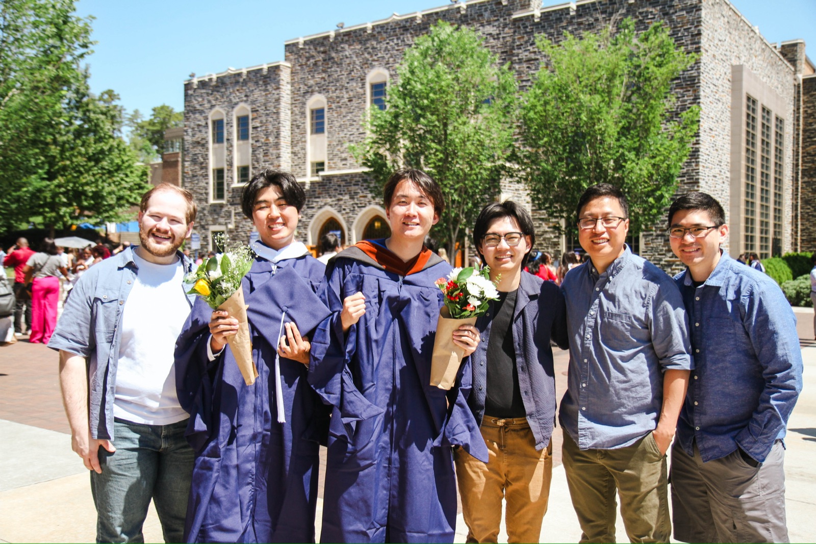 Han Zhang in a graduation gown with ISMP mentors and friends outside a Duke University building